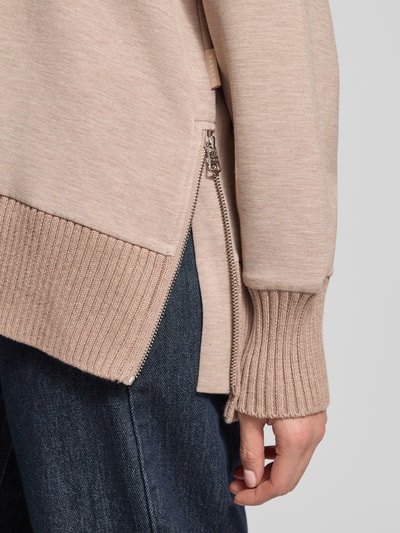Kobiece modelka ma na sobie Sweatshirt mit Stehkragen und überschnittenen Schultern od VARLEY, mieszanka wiskozy z dodatkiem streczu, krój relaxed fit, stójka, obniżone ramiona, beżowe odcienie, faktura dzianiny, detal zamka, detaliczne ujęcie rękawa.