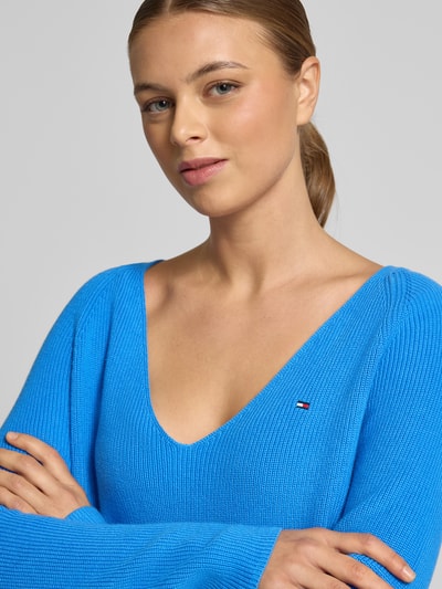 Kobiece modelka nosi Sweter z dzianiny Regular Fit Strickpullover aus reiner Baumwolle von Tommy Hilfiger, w paski, wyhaftowane logo, dekolt w serek, długi raglanowy rękaw, prążkowana faktura, bawełna, efekt: jednolity kolor, niebieski, zbliżenie na górną część ciała.