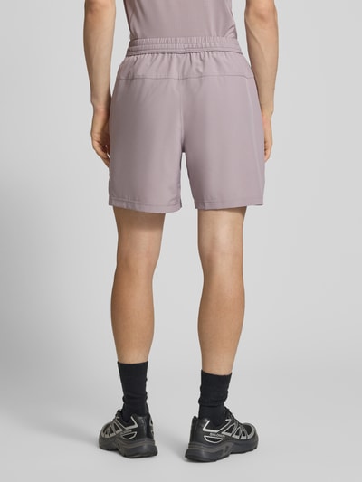 Mannenmodel draagt Shorts mit Logo-Print und Eingrifftaschen van NIKE TRAINING in lila met zij-steekzakken, recht model, elastische band met trekkoord, bandwijdte maat M 41 cm, binnenbeenlengte 19 cm. Ganzkörperansicht Rückansicht.