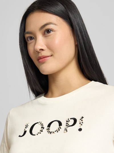 Frauenmodel trägt T-Shirt mit Label-Print Modell 'Tanna' von JOOP! aus reiner Baumwolle, Regular-Fit, Rundhalsausschnitt, Nahaufnahme Oberkörper.