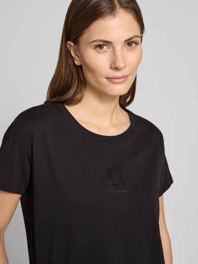 Frauenmodel trägt T-Shirt aus reiner Baumwolle von ARMANI EXCHANGE mit Strasssteinbesatz, Rundhalsausschnitt, schwarze Farbe, Nahaufnahme Oberkörper.