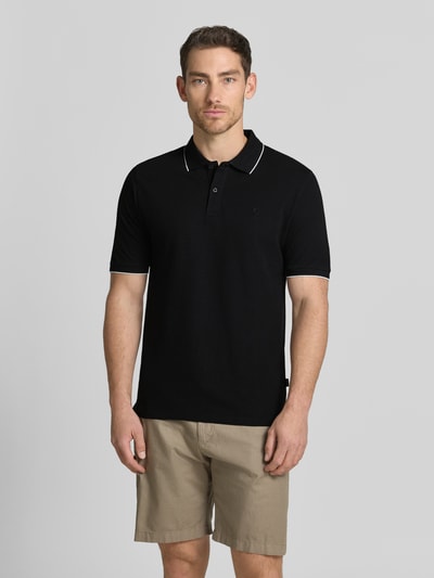 Męski model nosi Slim Fit Poloshirt mit Stitching von Jack & Jones Premium z bawełny, krój slim fit, haft, listwa guzikowa, długość tyłu w rozmiarze M: 70 cm, kolor czarny, beżowe szorty, całkowity widok z przodu.