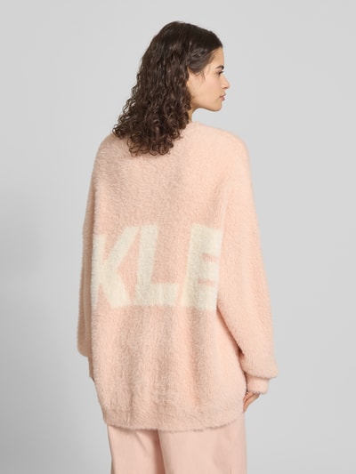 Frauenmodel trägt Oversized Strickpullover mit Label-Detail von Karo Kauer in zartem Rosa, lockere Passform, flauschige Textur, Rückansicht.