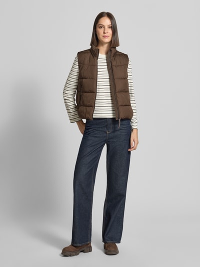 Frauenmodel trägt Regular Fit Weste in Stepp-Optik von camel active, braun, Zweiwege-Reißverschluss, Eingrifftaschen, Ganzkörperansicht von vorne. Rückenlänge 55 cm, Schulterbreite 39 cm, Brustweite 52 cm, Stehkragen, leicht glänzende Struktur, Damen Weste, KI-modifiziertes Bild.