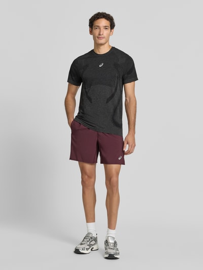Männermodel trägt Slim Fit RUNNING T-Shirt Modell 'ROAD' von ASICS in Dunkelgrau mit metallic Label-Print, Rundhalsausschnitt, Ganzkörperansicht von vorne.