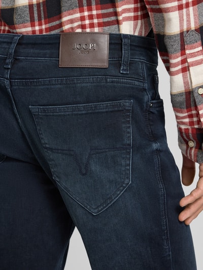 Männermodel draagt Jeans met 5-pocketmodel Model 'Mitch' van JOOP! Jeans in donker katoenmix met stretch, detailopname rug.