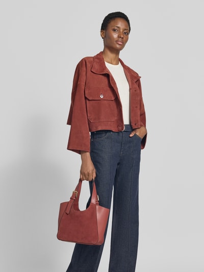 Frauenmodel trägt Tote Bag aus echtem Kalbsleder Modell 'Dora' von FURLA in Rotbraun mit Magnetverschluss und verstellbarem Schulterriemen, Ganzkörperansicht von vorne.