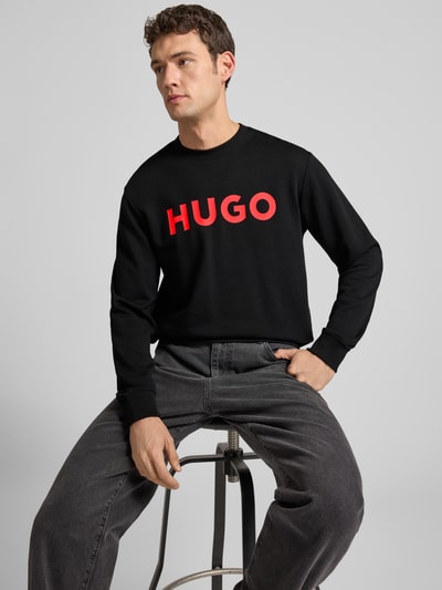 Męski model nosi czarne Sweatshirt mit Label-Detail Modell 'Dem' von HUGO z bawełny, luźny krój, czerwone logo, całkowity widok z przodu.