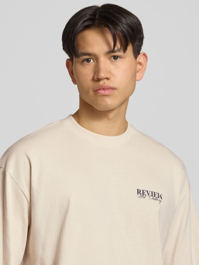 Männermodel trägt T-Shirt mit Logo-Print und Rundhalsausschnitt von REVIEW aus Reine Baumwolle, Loose-Fit, Nahaufnahme Oberkörper.