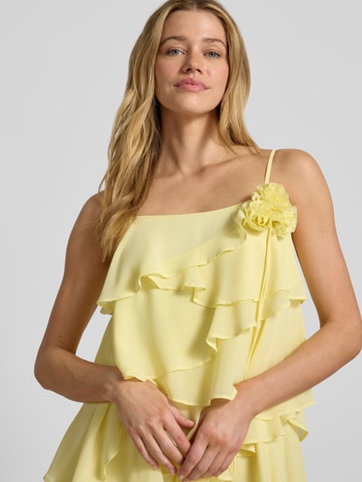Vrouwenmodel draagt Fließendes Cocktailkleid mit Volants Modell 'ALADYN' van Vero Moda, lichtgeel, effen, flowy fit, mini, rechte hals, sierbloem, volantdetails, verstelbare spaghettibandjes, close-up bovenlichaam.