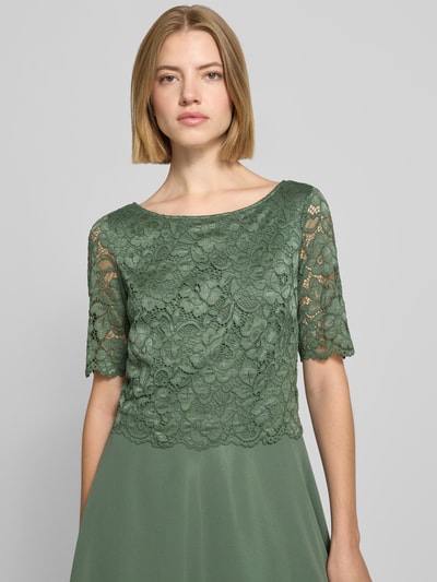 Frauenmodel trägt Tailliertes Cocktailkleid mit Spitzenbesatz von Vera Mont in dunklem Grün, florale Struktur, Nahaufnahme Oberkörper.