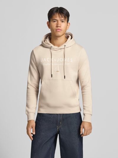 Männermodel trägt Relaxed Fit Hoodie aus Baumwoll-Mix Modell 'KYLE' von JACK & JONES in Beige mit Känguru-Tasche, Ganzkörperansicht von vorne.