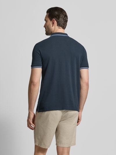 Męski model nosi Relaxed Fit Poloshirt mit Kontraststreifen od Lindbergh, bawełna, granatowy z białymi lamówkami, widok całej sylwetki z tyłu.