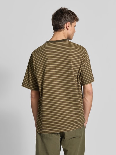 Männermodel trägt Relaxed Fit T-Shirt mit Label-Stitching von Forét in Olive mit feinen Streifen, reine Baumwolle, Ganzkörperansicht Rückansicht. Rückenlänge bei Größe M 73 cm, Halbarm, Rundhalsausschnitt.