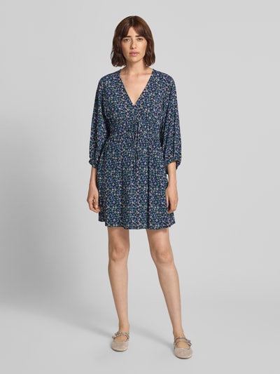 Frauenmodel trägt Minikleid aus reiner Viskose mit floralem Allover-Print von GAP, tailliert, V-Ausschnitt, 3/4-Arm, Ganzkörperansicht von vorne.