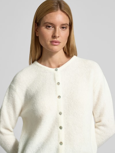 Frauenmodel trägt Strickjacke mit Woll-Anteil Modell 'VITOW' von American Vintage in Weiß, lockere Passform, Nahaufnahme Oberkörper. Elastischer Material-Mix, Rundhalsausschnitt, durchgehende Knopfleiste, gerippte Abschlüsse.