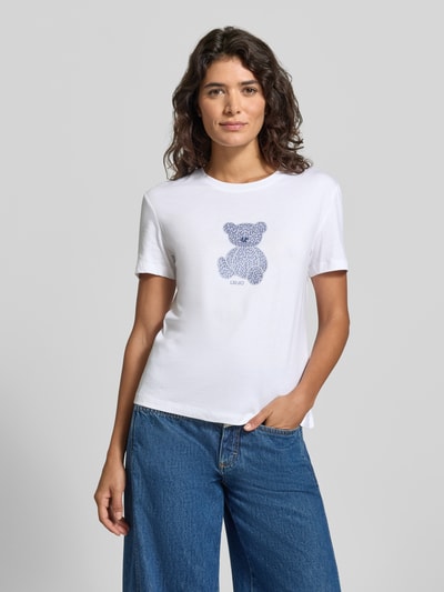 Kobiece model prezentuje Slim Fit T-Shirt mit Ziersteinbesatz od Liu Jo White, bawełna, motyw, okrągły dekolt, długość tyłu 57 cm, widok z przodu, zbliżenie na górną część ciała.
