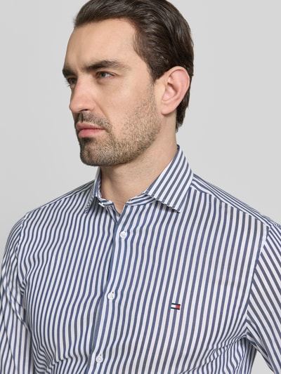 Männermodel trägt Slim Fit Businesshemd aus Baumwoll-Mix von Tommy Hilfiger Tailored, blau-weiß gestreift, Logo-Stitching, Nahaufnahme Oberkörper.