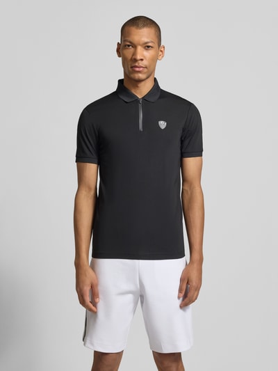 Männermodel trägt Slim Fit Poloshirt aus Viskose-Mix von EA7 Emporio Armani, schwarz, Logo-Detail, elastische Ärmel, Ganzkörperansicht von vorne.