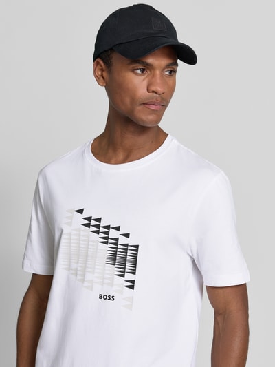 Męski model nosi Relaxed Fit T-Shirt aus Baumwoll-Mix Modell 'TS_NETWORK FLAG' od BOSS Green, biała koszulka z czarnym nadrukiem geometrycznym na piersi, widok na górną część ciała z przodu.
