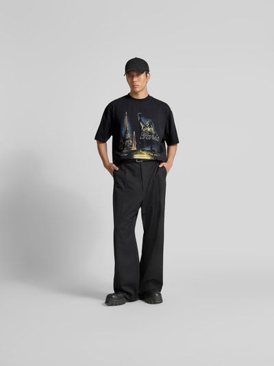 Männermodel trägt Relaxed Fit T-Shirt aus Baumwolle von VETEMENTS mit Motiv-Print, Rundhalsausschnitt, schwarze Farbe, Ganzkörperansicht von vorne.