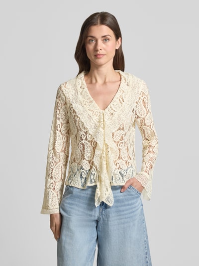 Modelka nosi Regular Fit Regular Fit aus Baumwoll-Mix Modell 'SALLY' od Vero Moda, półprzezroczysta bluzka damska z abstrakcyjnym wzorem, koronkową teksturą, długim rękawem, głębokim dekoltem V i falistym kołnierzem, kremowo-beżowe odcienie, widok całej sylwetki z przodu.