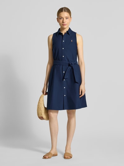 Vrouwenmodel draagt Regular Fit Polokleid aus reiner Baumwolle van Polo Ralph Lauren in look: effen, knielang, hooggesloten hals, gestikt logo, knoopsluiting, tailleriem, mouwloos, materiaal: puur katoen, ganzlichaamsaanzicht van voren.