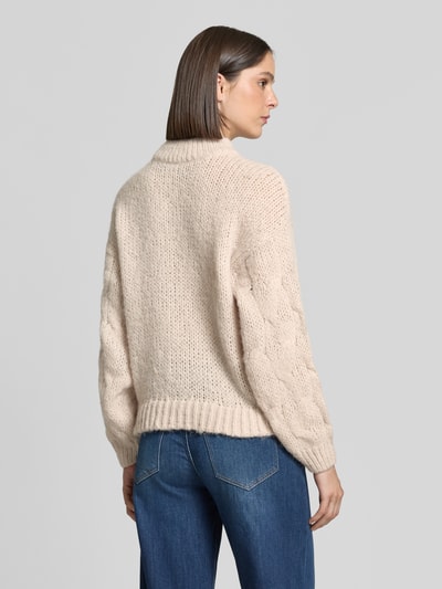 Frauenmodel trägt cremefarbenen Regular Fit Pullover mit Rundhalsausschnitt Modell 'MAYBE' von VERO MODA, grobe Strickstruktur, Ganzkörperansicht Rückansicht.