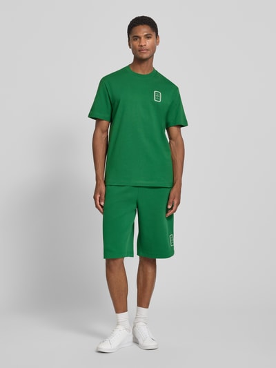 Männermodel trägt grünes Regular Fit T-Shirt aus reiner Baumwolle Modell 'CN Tenniscourt Backprint' von Lacoste, Ganzkörperansicht von vorne, Herren T-Shirt.