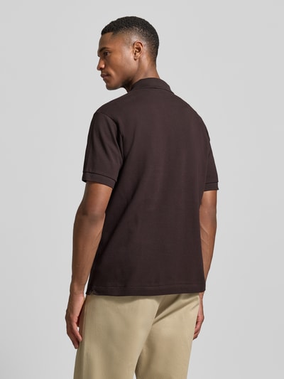 Männermodel trägt Regular Fit Poloshirt aus reiner Baumwolle von Lacoste in Dunkelbraun, Piqué-Struktur, unifarben, Ganzkörperansicht Rückansicht.