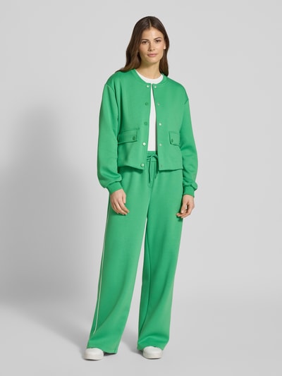 Frauenmodel trägt Regular Fit Jacke mit Viskose-Anteil Modell 'Kate' von ICHI in kräftigem Grün, elastischer Material-Mix, Stehkragen, Pattentaschen, durchgängige Knopfleiste, elastische Ärmelabschlüsse, Ganzkörperansicht von vorne.