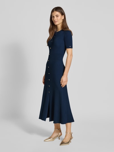 Frauenmodel trägt Eng anliegendes Freizeitkleid aus Viskose-Mix von Tommy Hilfiger, Optik: Unifarben, Passform, Midi-Länge, Rundhals, Logo-Detail, Zierknöpfe, Knopfleiste, Kurzarm, dunkles Blau, strukturierte feine Rippen, fließender Stoff, Ganzkörperansicht von vorne.
