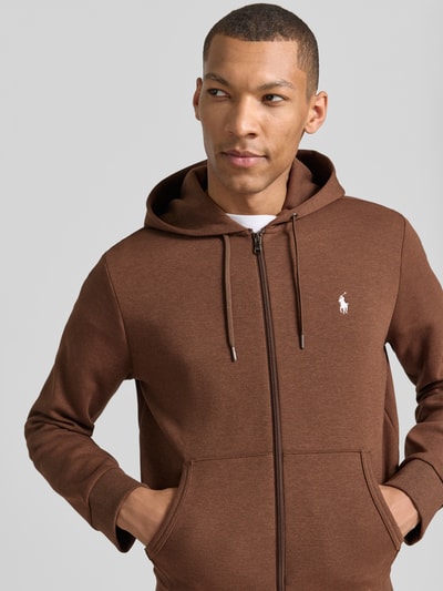 Męski model nosi Regular Fit Sweatjacke aus Baumwoll-Mix od Polo Ralph Lauren, brązowy kolor, kieszenie, logo, krój regular fit, bluza z kapturem, zamek błyskawiczny, detal z haftowanym logo, z bawełnianego miksu, widok na górną część ciała z przodu.