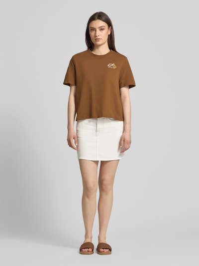Frauenmodel trägt Relaxed Fit T-Shirt aus reiner Baumwolle - Special Drop von Marc O’Polo Denim in Braun mit Motiv-Print, unifarben, Rundhalsausschnitt, kurzarm, kombiniert mit weißem Rock, Ganzkörperansicht von vorne.
