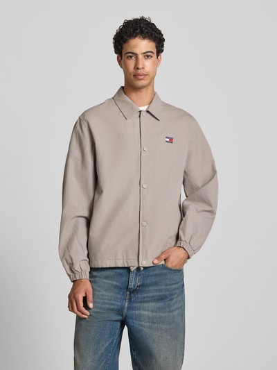 Männermodel trägt Regular Fit Hemdjacke aus reiner Baumwolle von Tommy Jeans in Optik: Unifarben mit Umlegekragen, Druckknopfleiste, Label-Stitching-Applikation, Eingrifftaschen, Langarm, Ganzkörperansicht von vorne.
