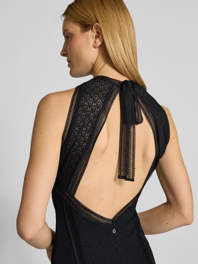 Kobiece modelka nosi długą sukienkę Maxikleid mit Spitze und Gehschlitz Modell 'NEW LIZA' od Guess, czarny półprzezroczysty materiał, koronka, okrągły dekolt, wiązanie oraz wycięcie na plecach, detal z logo z tyłu, halka pod sukienkę, mieszanka materiałów z dodatkiem streczu; zbliżenie na górę pleców