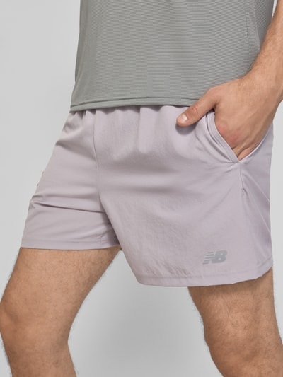 Männermodel trägt Shorts mit elastischem Bund und Logo von New Balance in Hellgrau, Regular Fit, Logo auf dem Bein, Nahaufnahme Oberkörper.