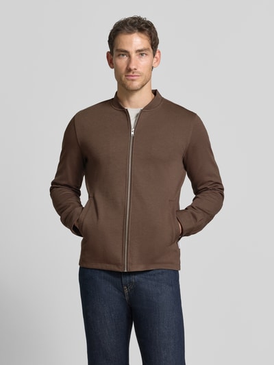 Męski model nosi Slim Fit Sweatjacke mit Stehkragen von Lindbergh, mieszanka materiałów z dodatkiem streczu, krój slim fit, stójka, zamek błyskawiczny, boczne wpuszczane kieszenie, długość tyłu w rozmiarze M: 67 cm, długość rękawów w rozmiarze M: 66 cm, brązowy kolor, gładka faktura, widok całej sylwetki z przodu.