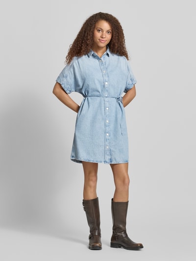 Kobiece model nosi Relaxed Fit Jeanskleid aus reiner Baumwolle von Marc O'Polo Denim, tkanina stylizowana na denim, krój relaxed fit, długość mini, wysokie zapięcie, kołnierzyk koszulowy, wiązany pasek, zapięcie na guziki, krótki rękaw, 100% bawełna, jasnoniebieski, gładka faktura, Ganzkörperansicht von vorne.