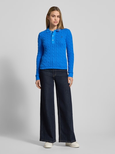 Frauenmodel trägt Strickpullover mit Zopfmuster und Polokragen von Polo Ralph Lauren in Blau, kombiniert mit dunkler Jeans, Ganzkörperansicht von vorne, Slim Fit, reine Baumwolle, Label-Stitching.