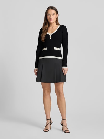 Frauenmodel trägt Slim Fit Longsleeve aus Viskose-Mix Modell 'Laurel' von Guess, schwarz mit Strick-Optik und Zierknöpfen, Ganzkörperansicht von vorne.
