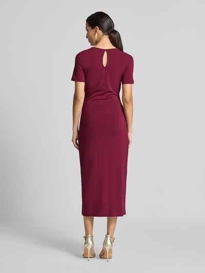 Frauenmodel trägt Midikleid mit Zierschnalle Modell 'Justine' von VILA in Dunkelrot, elastischer Stoff, tailliert, Ganzkörperansicht Rückansicht.