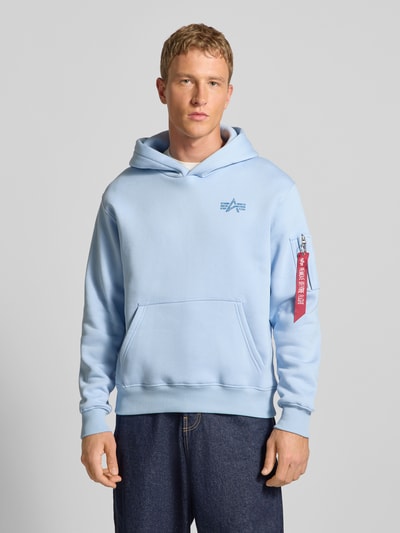 Männermodel trägt Hoodie mit Label-Details von Alpha Industries, hellblau, Baumwoll-Mix, Känguru-Tasche, Lockerer-Schnitt, Ganzkörperansicht von vorne.