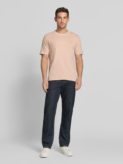 Männermodel trägt T-Shirt mit Label-Print Modell 'FELIX' von Jack & Jones Premium, reine Baumwolle, Regular Fit, Rundhalsausschnitt, hellrosa Farbton, kombiniert mit dunkler Jeans und weißen Sneakers, Ganzkörperansicht von vorne.