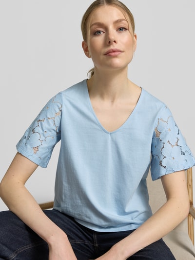 Frauenmodel trägt Regular Fit Blusenshirt aus reiner Baumwolle Modell 'VILLA' von Vero Moda, unifarben hellblau mit Spitzenbesatz an den kurzen Ärmeln, V-Ausschnitt, Jersey-Struktur, Nahaufnahme Oberkörper.