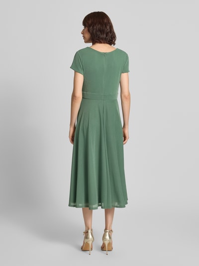 Frauenmodel trägt Tailliertes Cocktailkleid mit V-Ausschnitt von Vera Mont in sanftem Grün, fließender Stoff, Ganzkörperansicht Rückansicht.