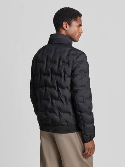 Männermodel trägt Regular Fit Bomberjacke mit reflektierenden Details von Tom Tailor in Schwarz, klare Steppstruktur, Ganzkörperansicht Rückansicht. Herren Bomberjacke / Blouson