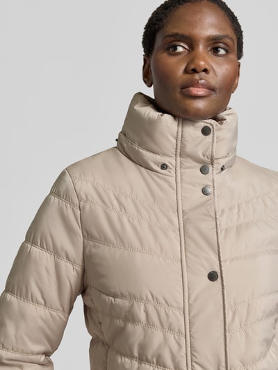 Modelka nosi kurtkę 'Jacke in Stepp-Optik mit Kapuze' od FUCHS SCHMITT w kolorze beżowym, z efektem pikowania, taliowany krój, kaptur, ocieplany stójka, wpuszczane kieszenie z zamkiem błyskawicznym, szerokość ramion w rozmiarze 36: 40 cm, szerokość klatki piersiowej w rozmiarze 36: 48 cm, długość rękawa w rozmiarze 36: 64 cm, długość tyłu w rozmiarze 36: 74 cm, zbliżenie na górną część ciała.