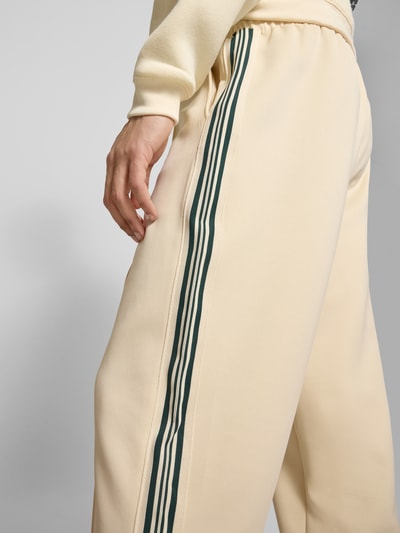 Männermodel trägt Regular Fit Sweatpants mit elastischem Bund Modell 'RIBER' von Only & Sons in Beige mit grünen Kontraststreifen, feine Webstruktur, Nahaufnahme Oberschenkel und Bund seitlich.