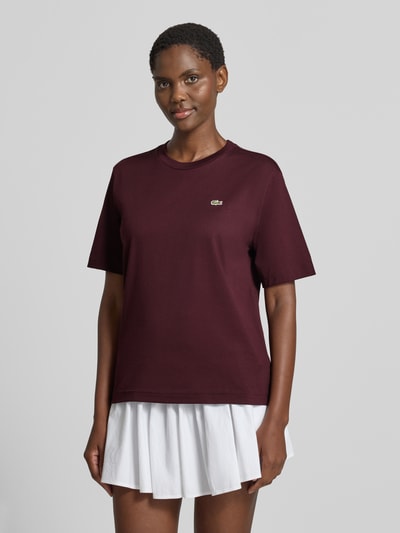 Frauenmodel trägt Relaxed Fit T-Shirt aus reiner Baumwolle von Lacoste in Dunkelrot mit glatter Textur, Ganzkörperansicht von vorne.